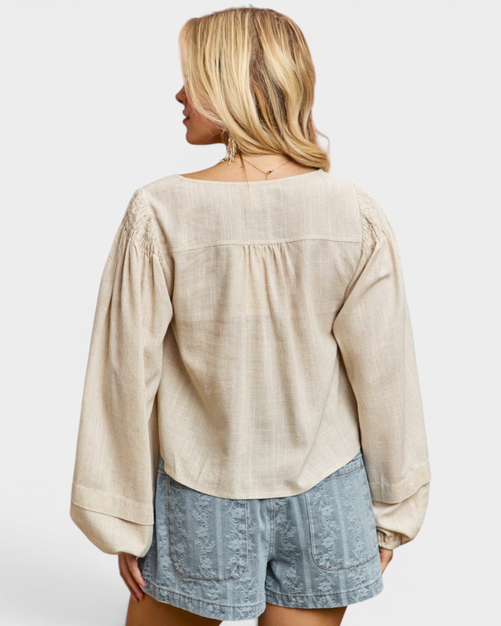 Woman wearing a beige blouse and denim shorts on a white background