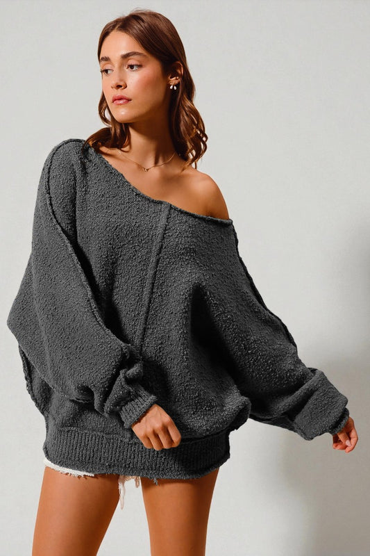 Woman wearing a gray oversized sweater against a plain background