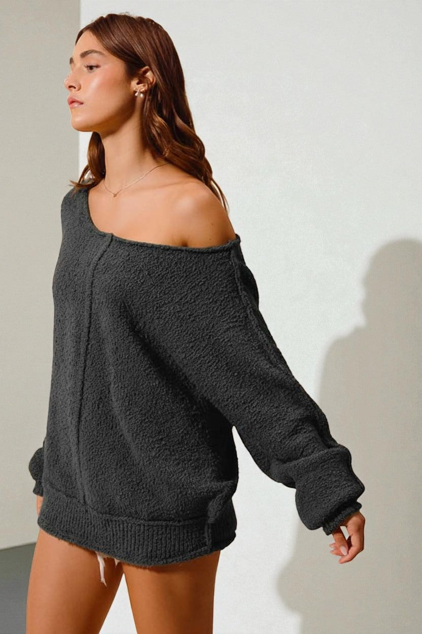 Woman wearing a dark gray off-shoulder sweater and shorts against a plain background