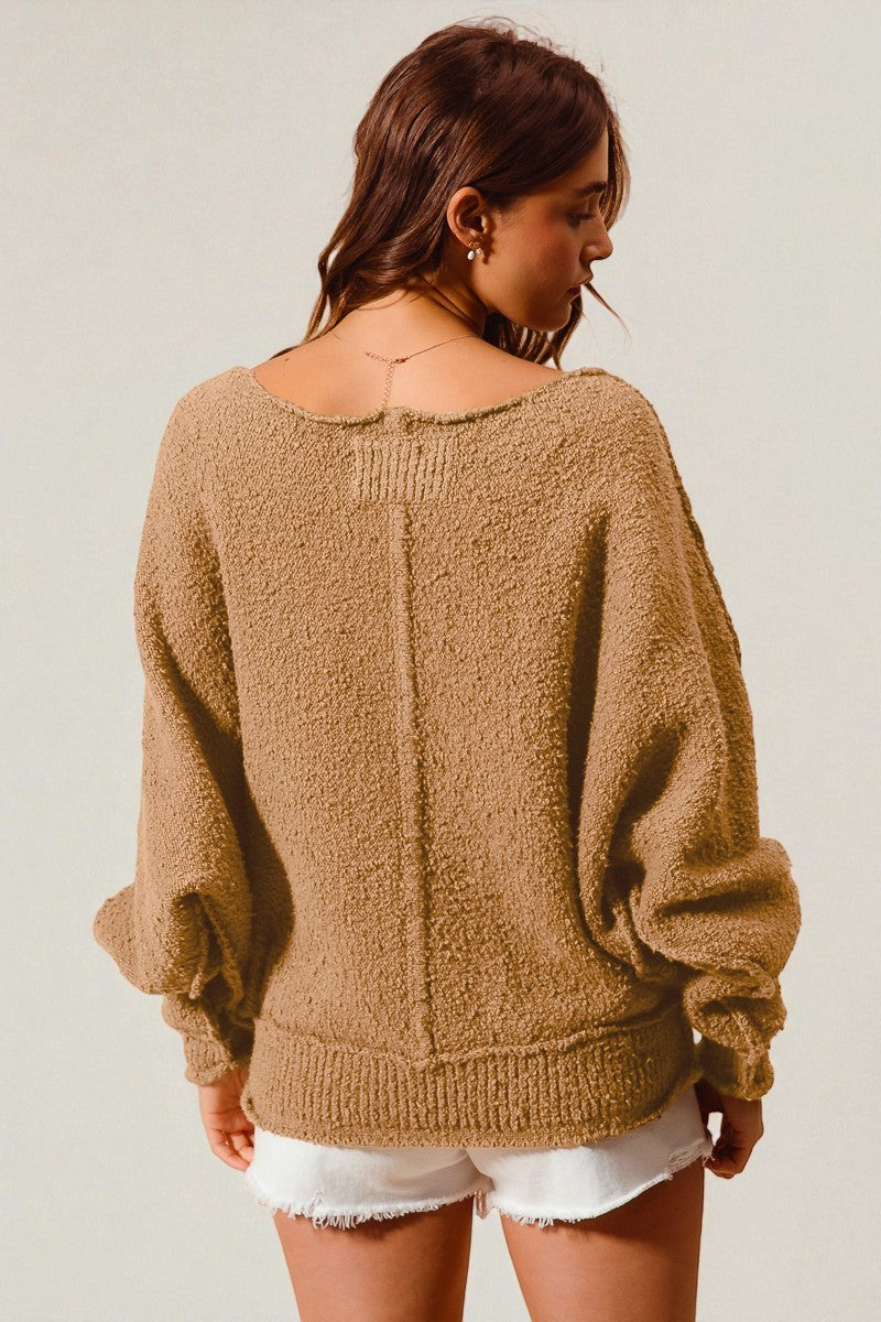 Woman wearing a brown sweater and white shorts against a plain background