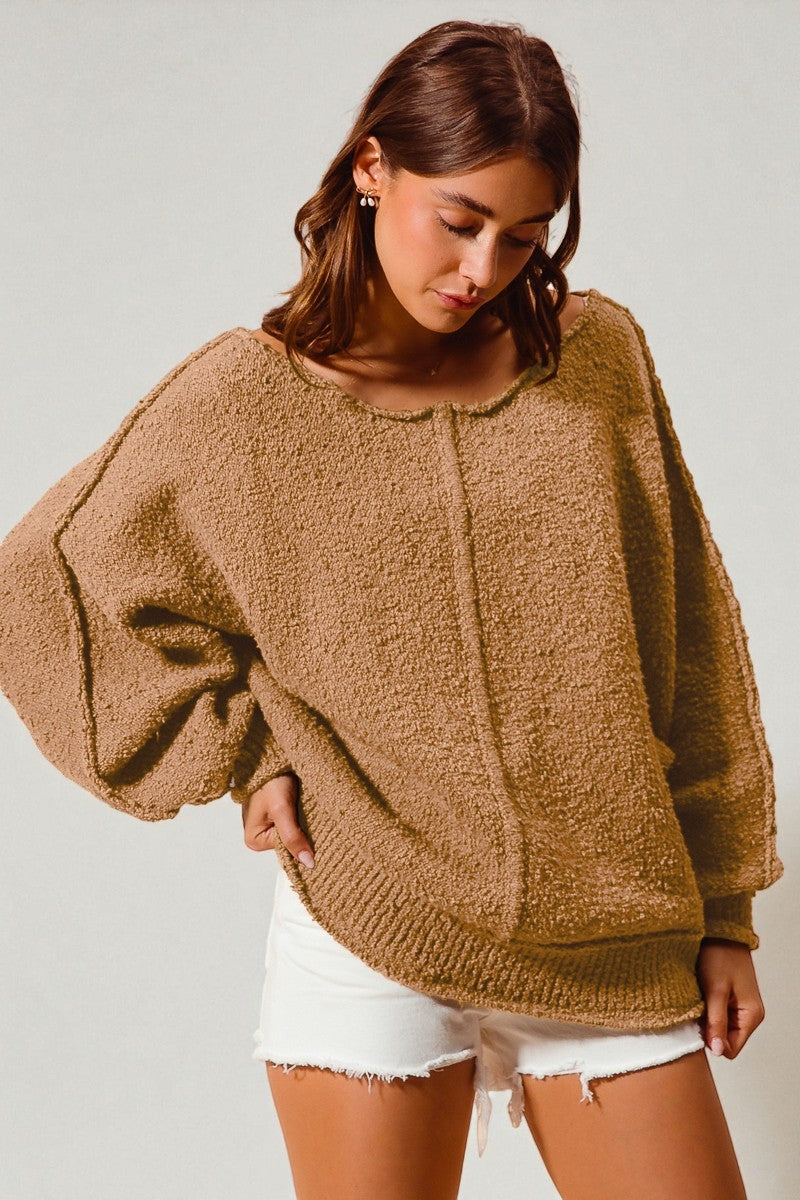 Woman wearing a brown oversized sweater and white shorts on a plain background
