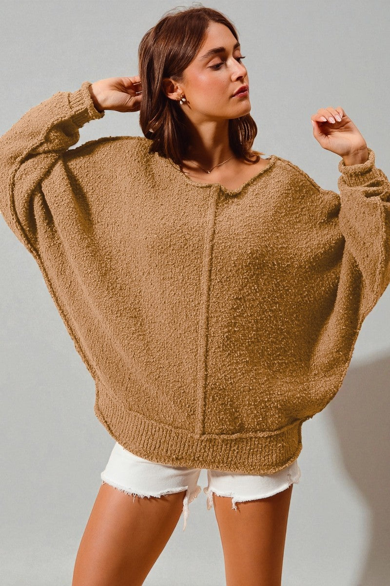 Woman wearing a brown fuzzy sweater and white shorts against a plain background