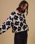 Woman wearing a black and white floral patterned sweater against a beige background
