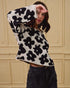 Person wearing a black and white floral patterned sweater against a beige wall.