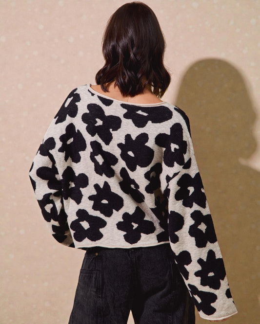 Person wearing a black and white floral patterned sweater against a beige background