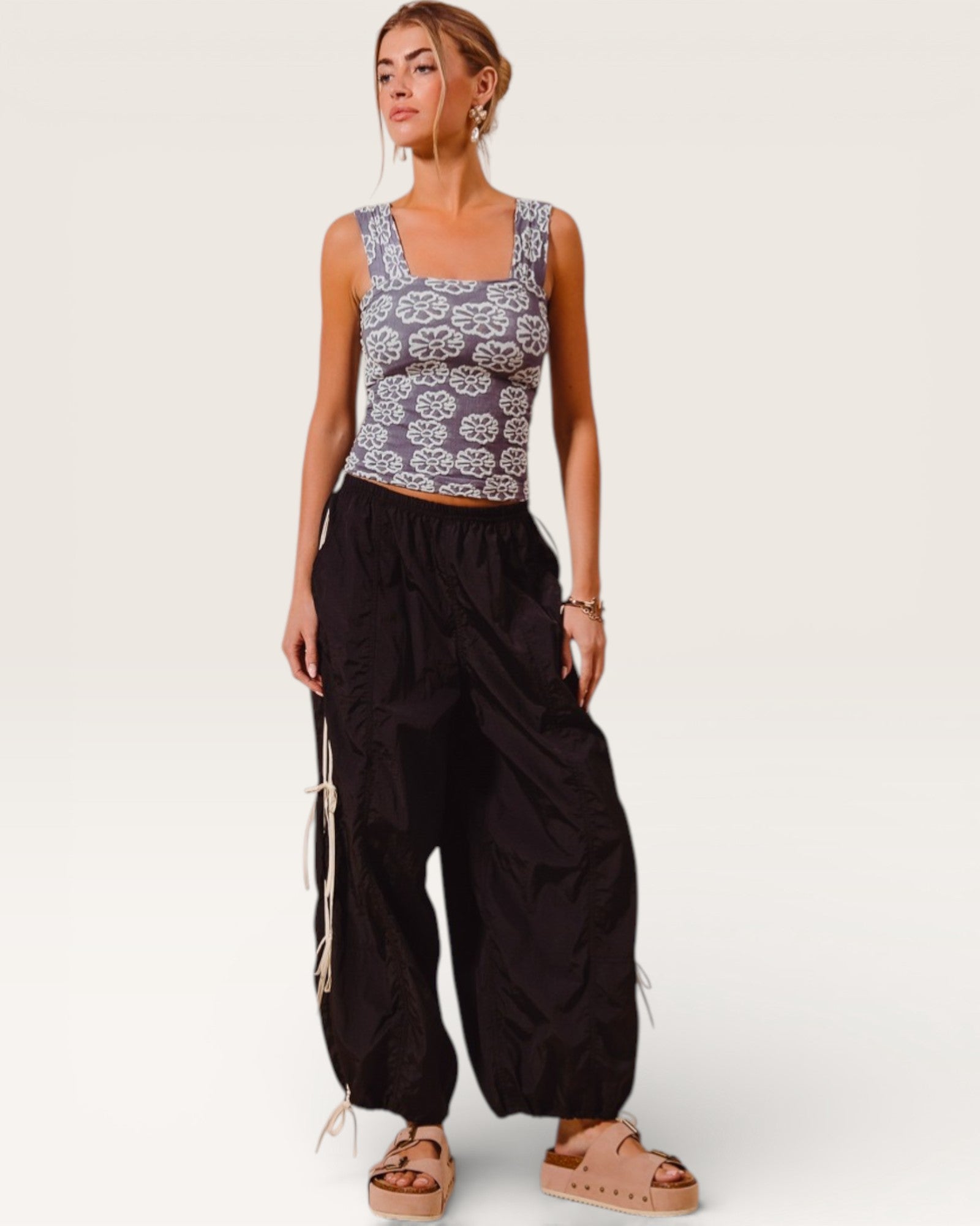 Woman wearing a patterned tank top and black wide-leg pants on a white background