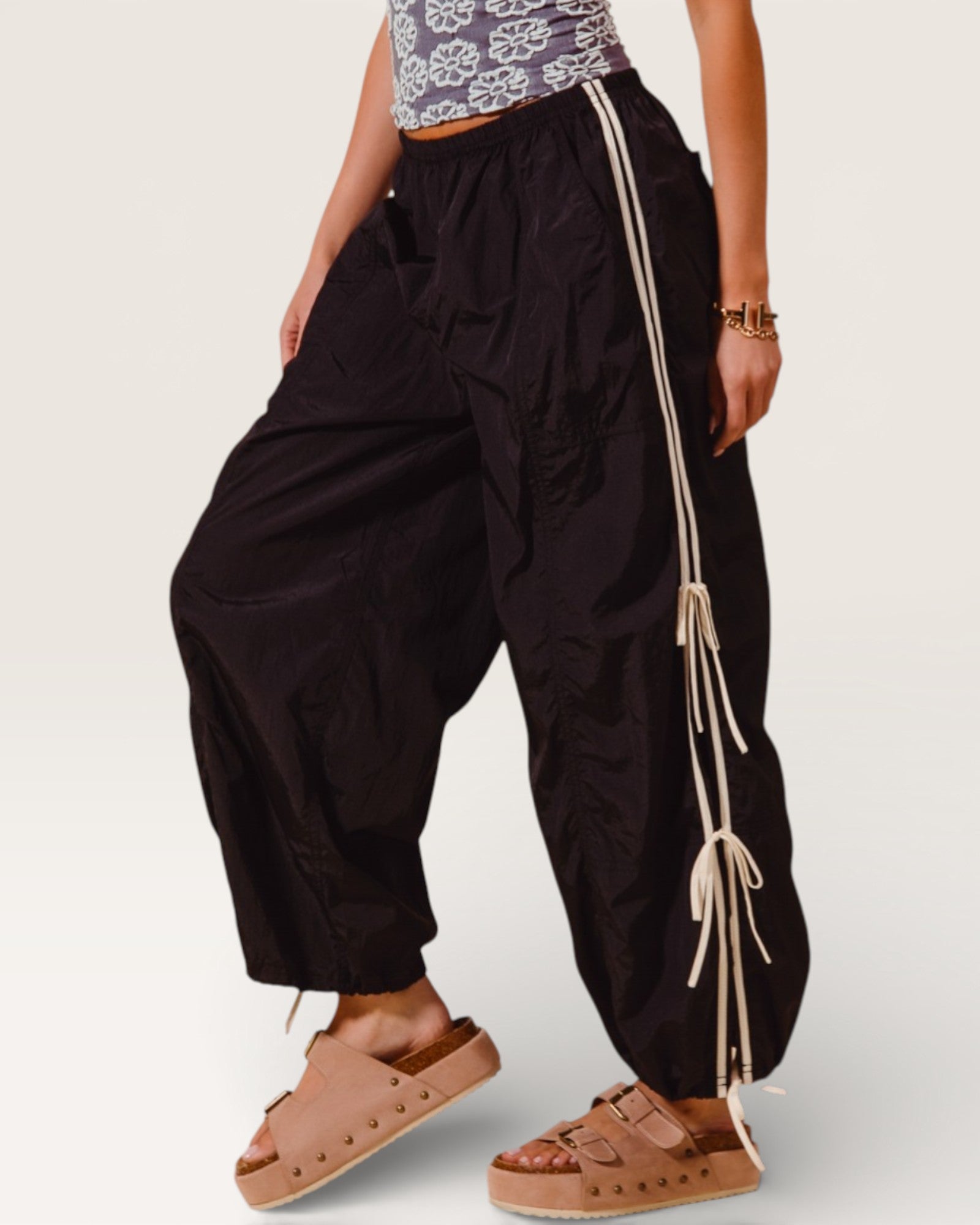 Person wearing black wide-leg pants with drawstrings and brown sandals on a plain background