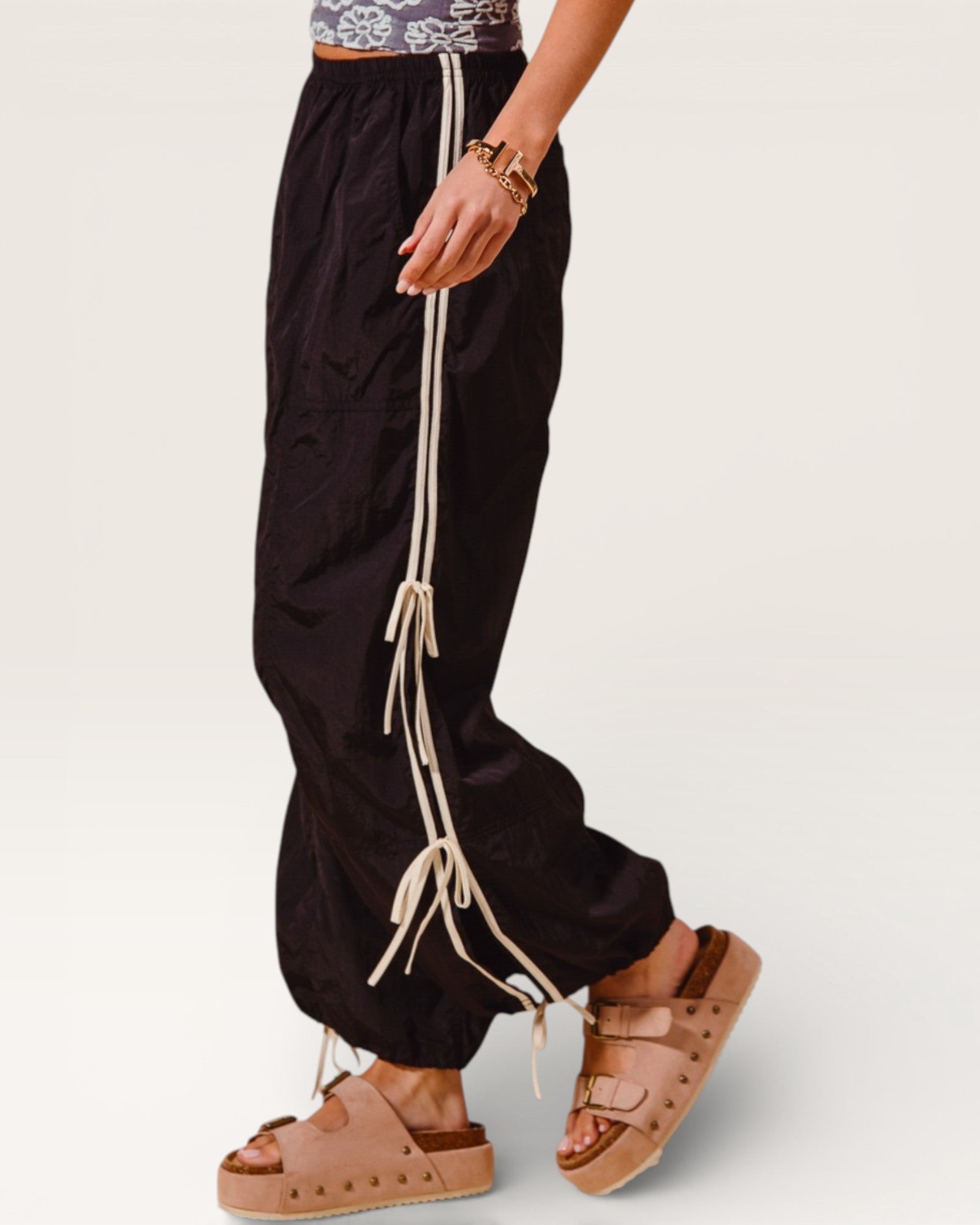Person wearing black pants with beige drawstrings and brown sandals on a white background