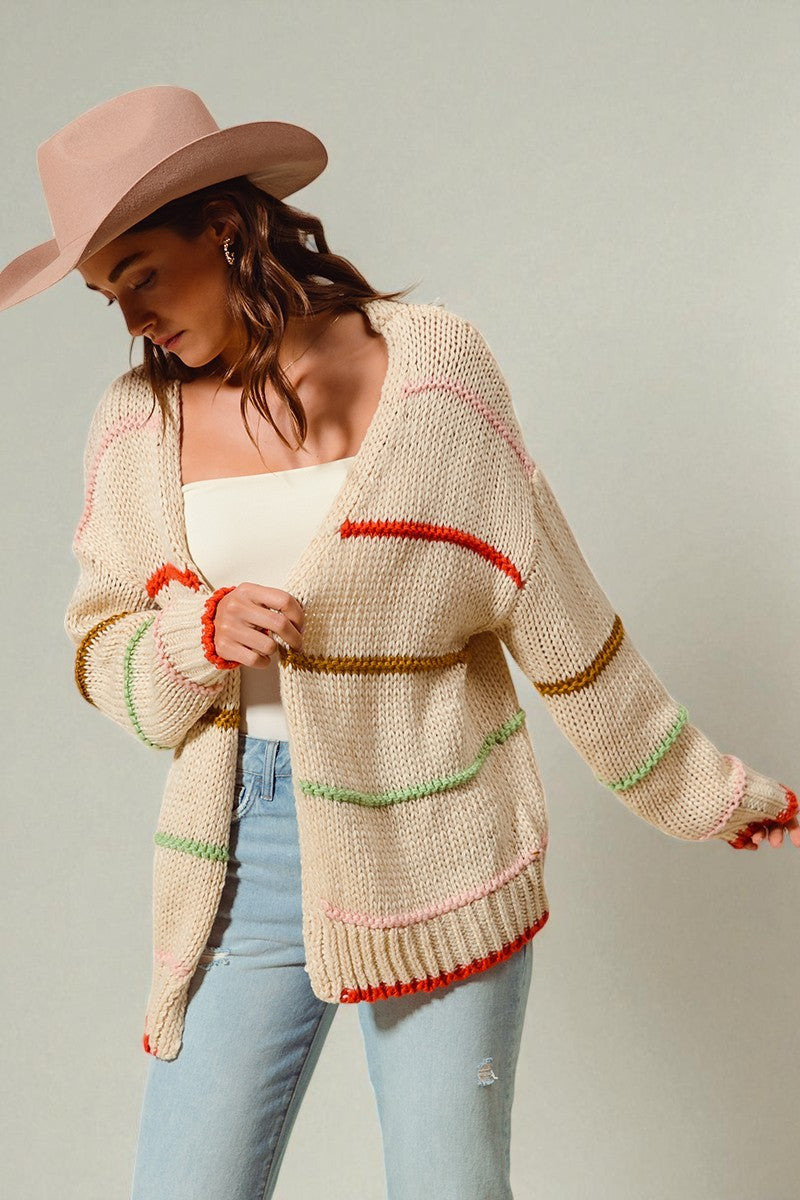 Woman wearing a patterned cardigan with colorful trim on a plain background