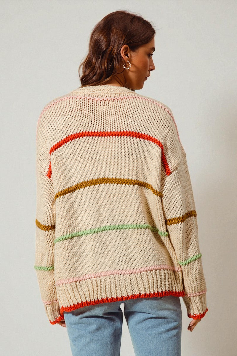 Person wearing a beige sweater with colorful stripes on a plain background