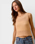 Woman wearing a beige knitted tank top and blue jeans on a plain background