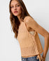 Woman wearing a beige ribbed tank top against a plain background