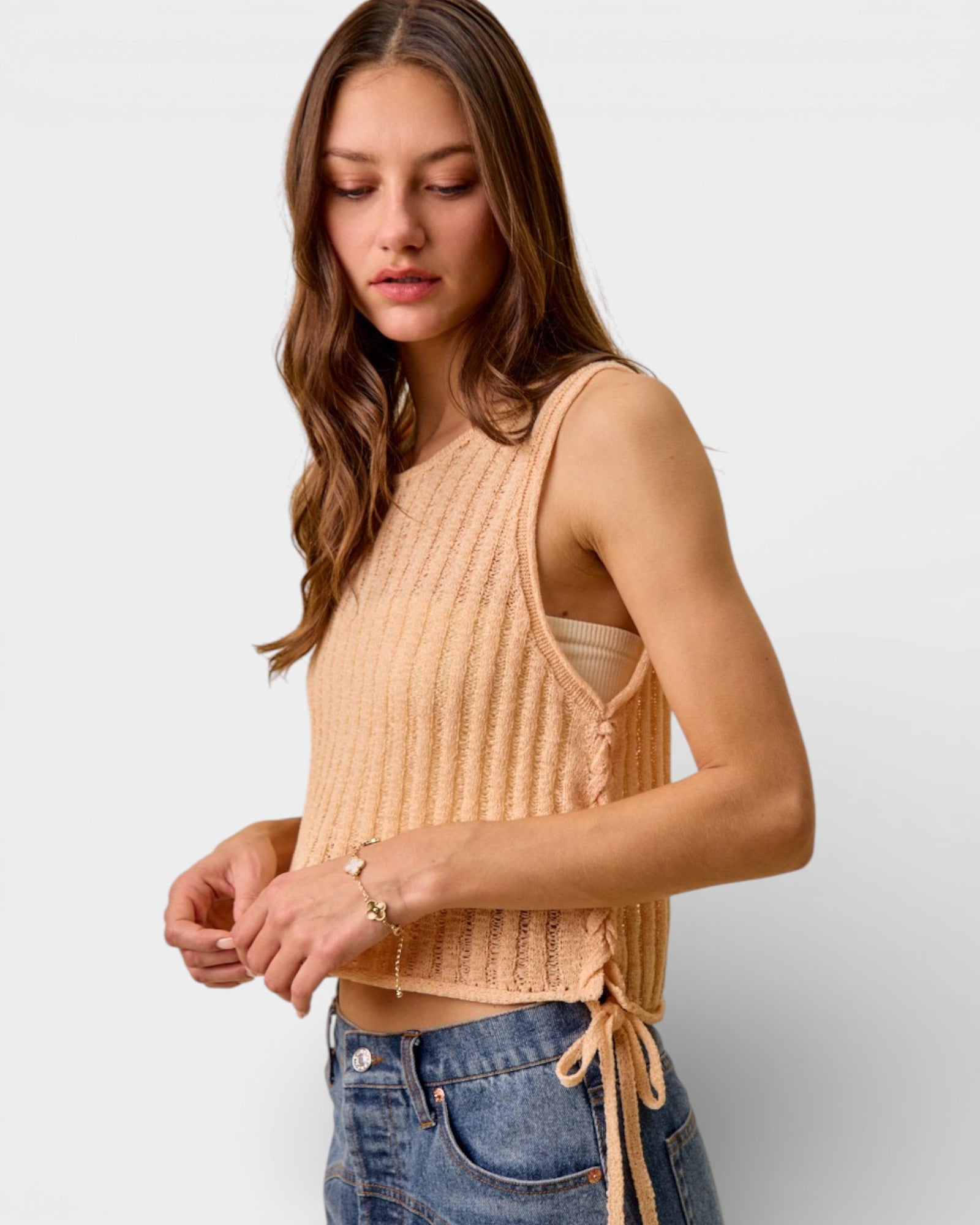 Woman wearing a beige knitted tank top with denim shorts on a light gray background
