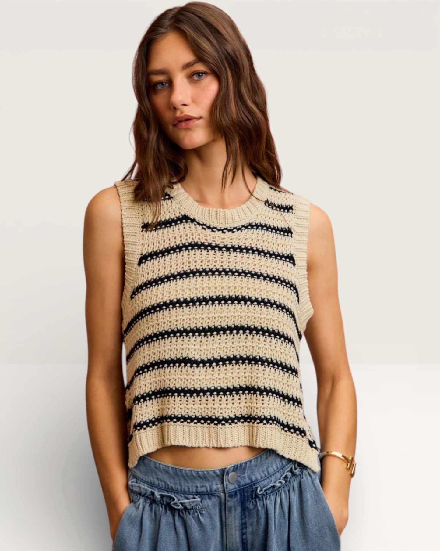 Woman wearing a striped sleeveless top and denim pants on a plain background