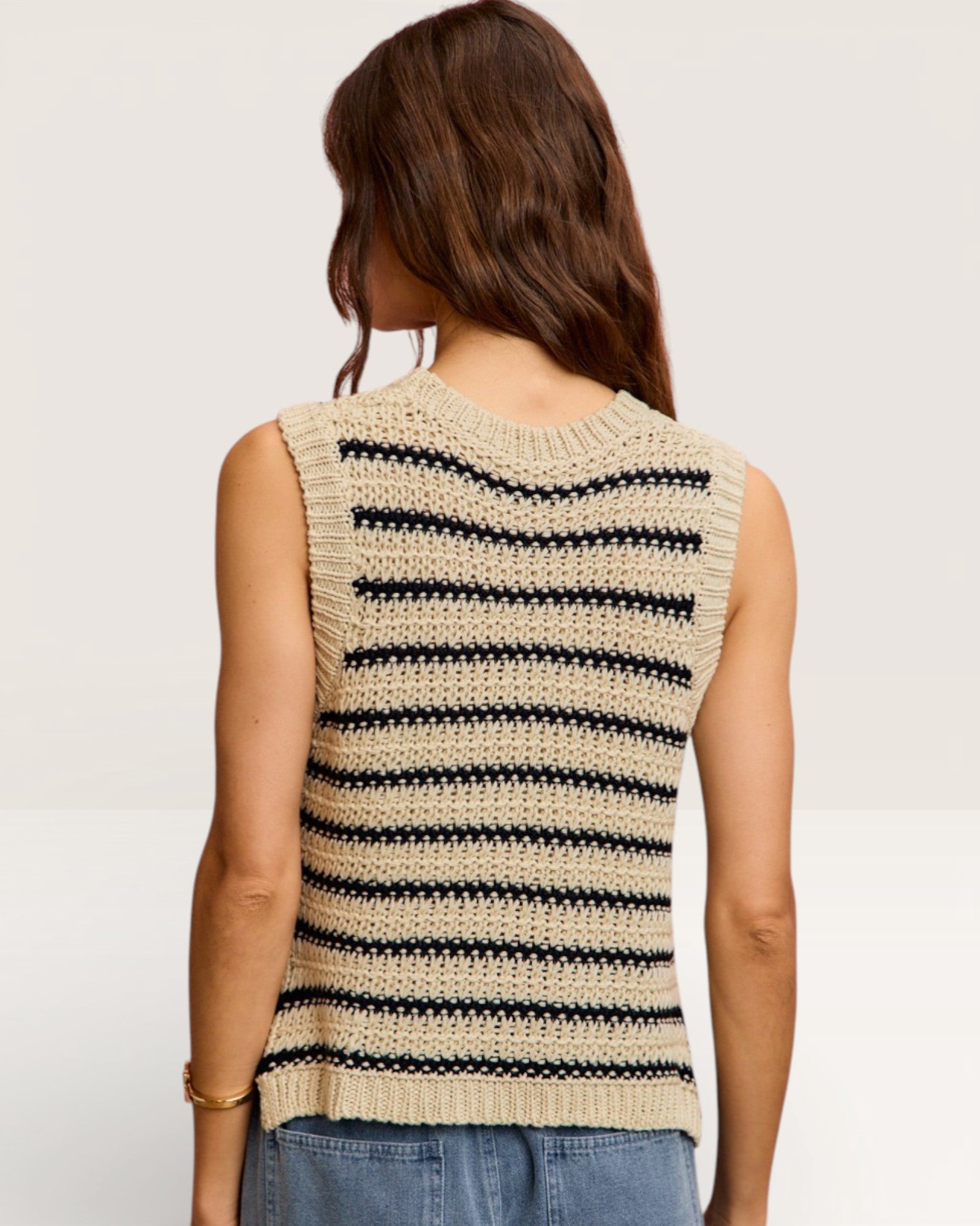 Woman wearing a beige sleeveless knitted top with black stripes on a plain background
