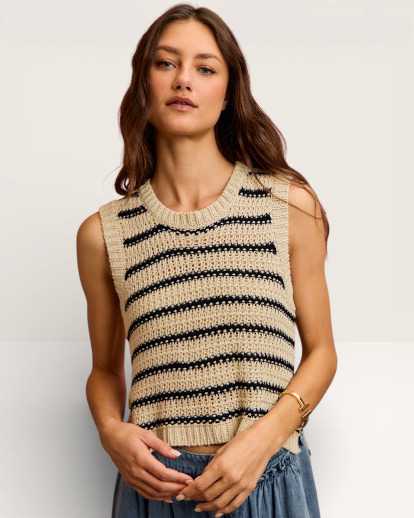 Woman wearing a beige and black striped sleeveless sweater against a plain background