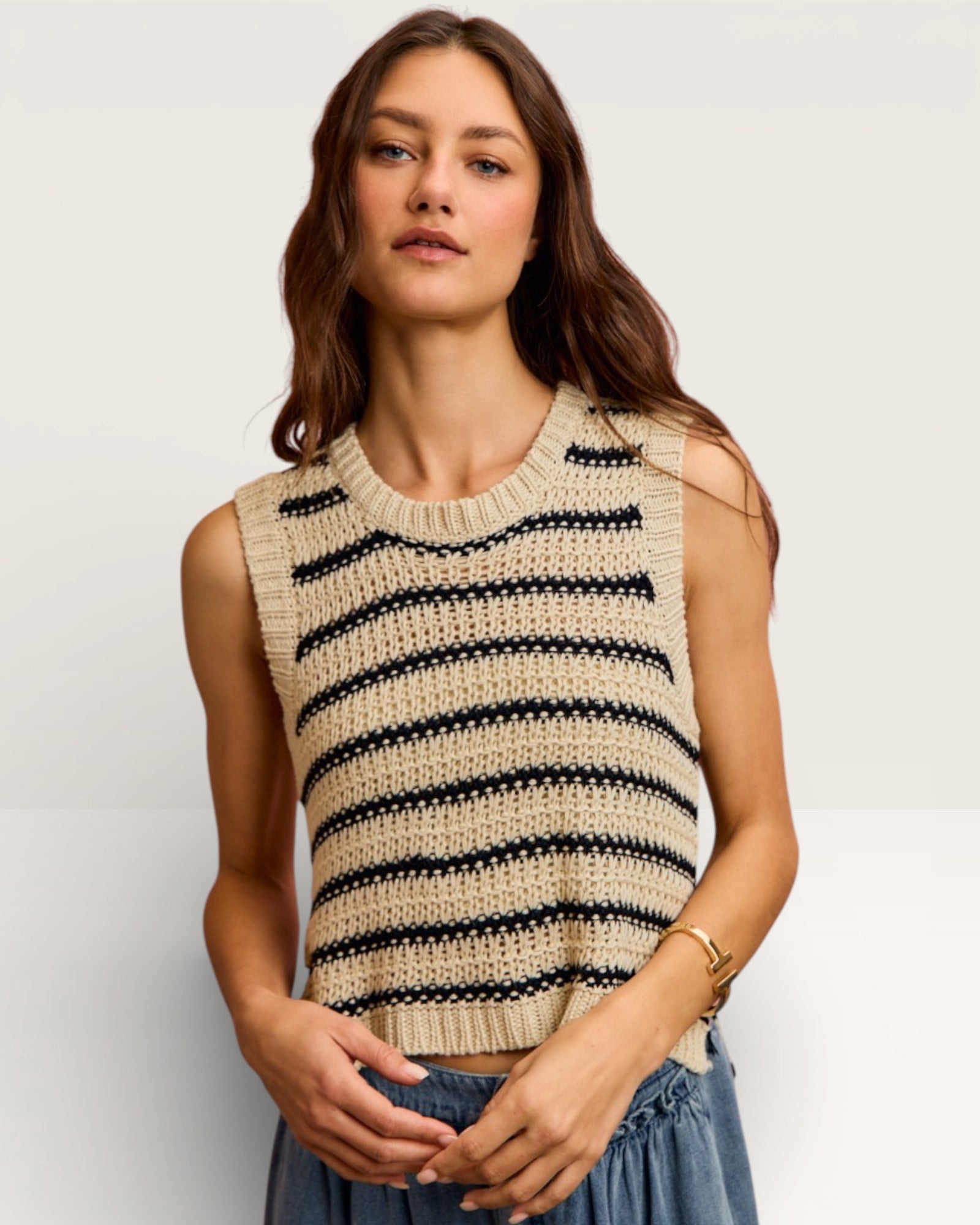 Woman wearing a beige and black striped sleeveless sweater against a plain background