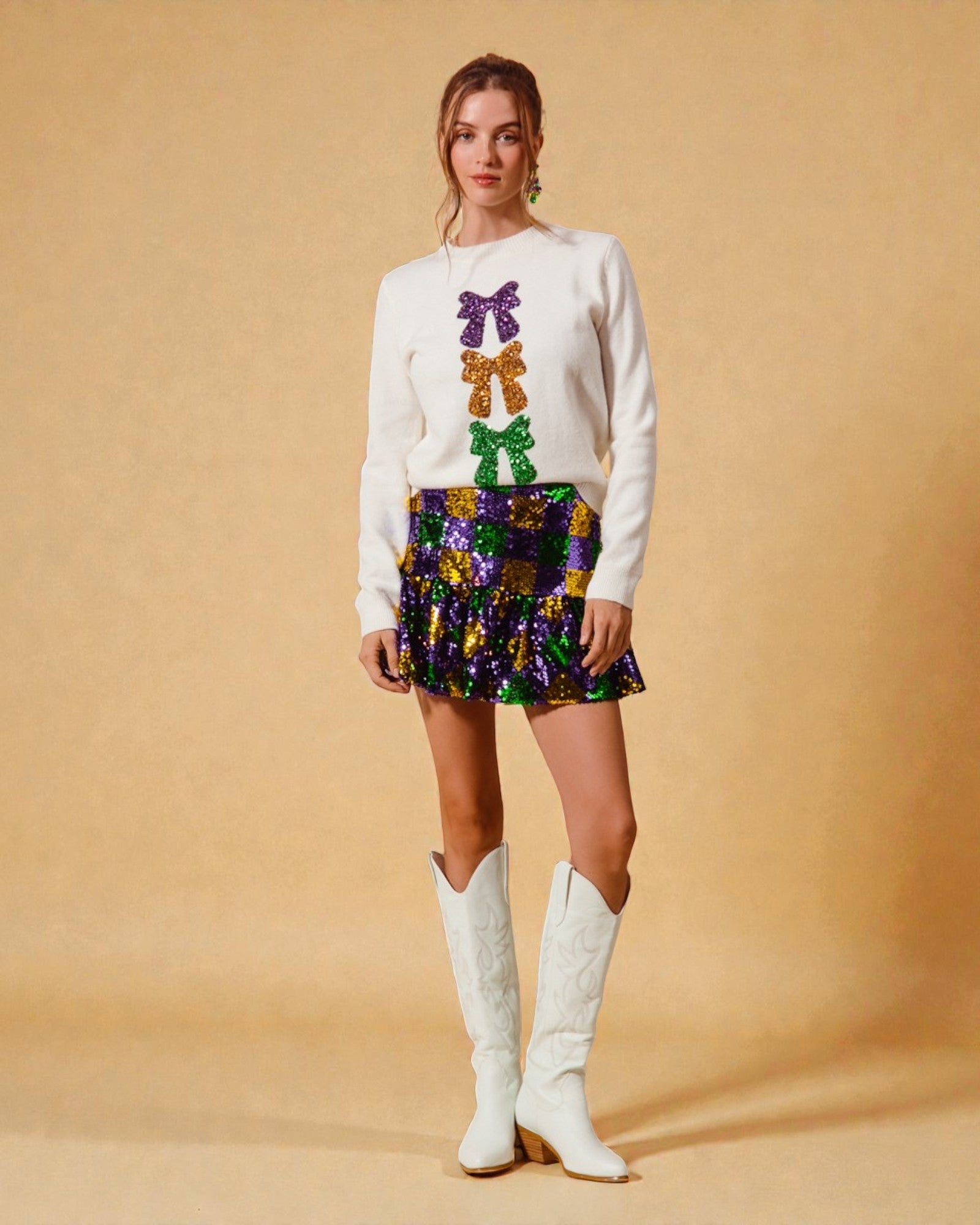 Woman wearing a white sweater with colorful butterfly patterns, a patterned skirt, and white knee-high boots on a beige background.