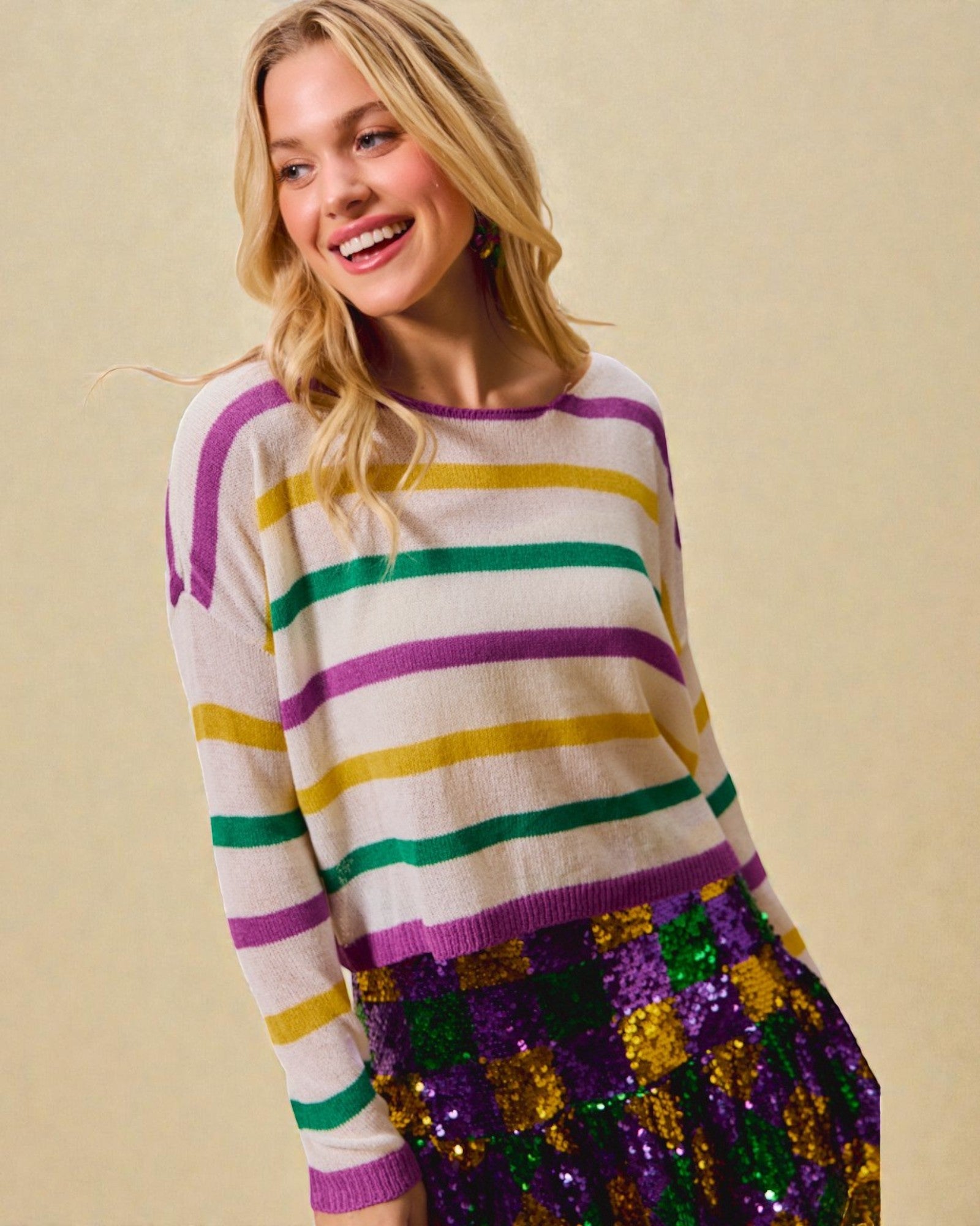 Woman wearing a colorful striped sweater and sequin skirt against a beige background