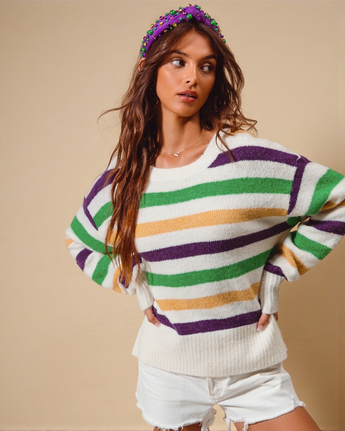 Woman wearing a colorful striped sweater and headband against a beige background
