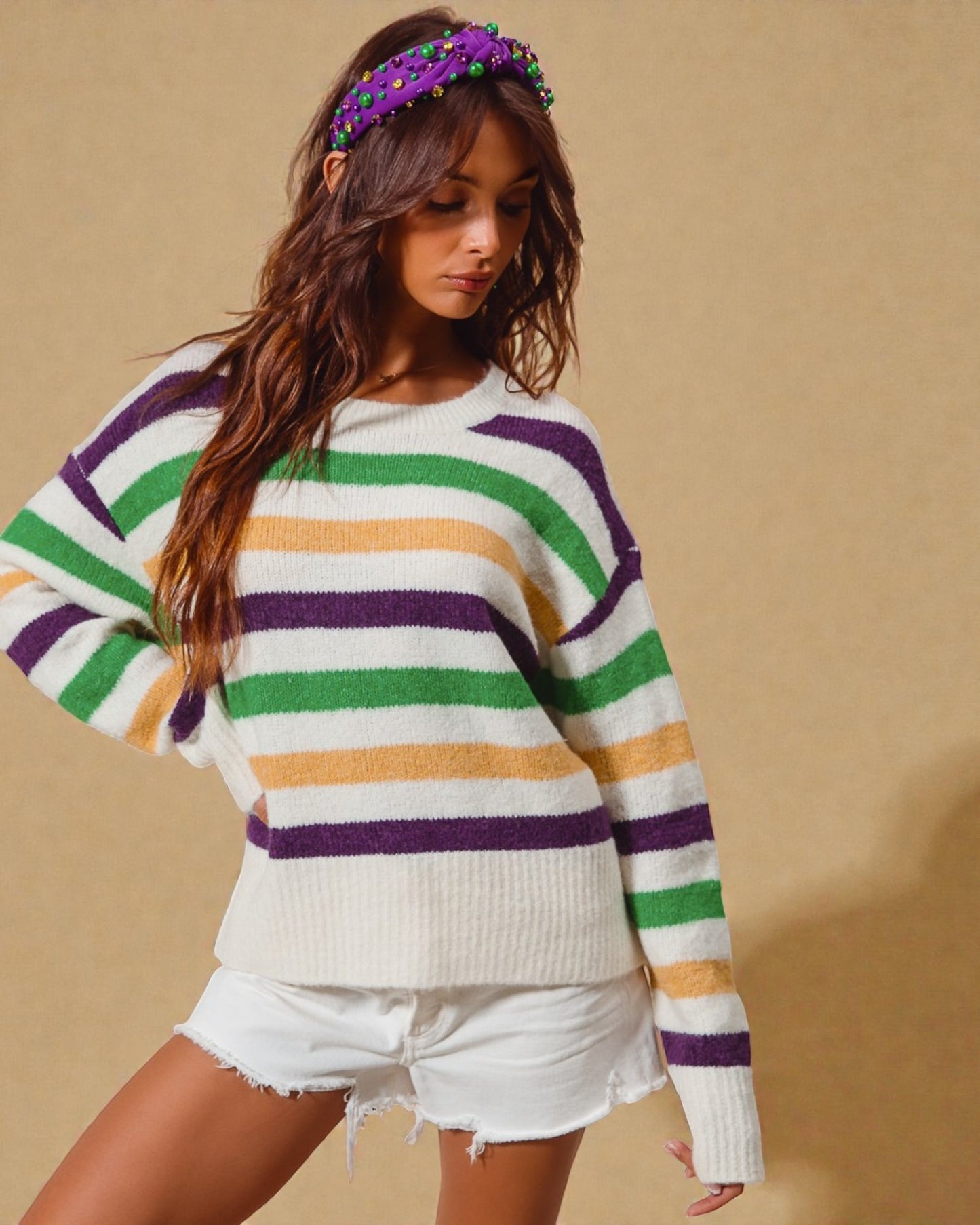 Woman wearing a colorful striped sweater and white shorts against a beige background