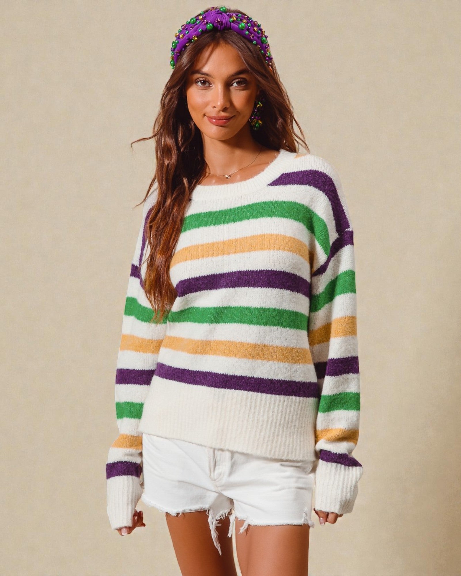 Woman wearing a colorful striped sweater and white shorts with a neutral background