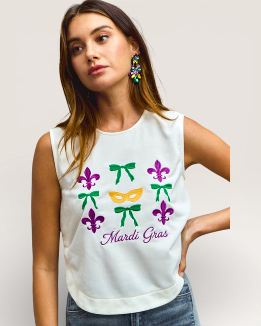 Woman wearing a white sleeveless top with Mardi Gras-themed designs on a plain background