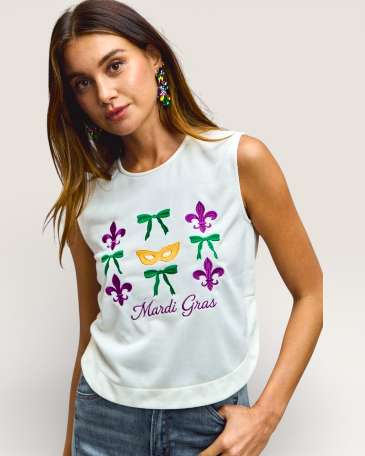 Woman wearing a white sleeveless top with Mardi Gras-themed designs on a plain background