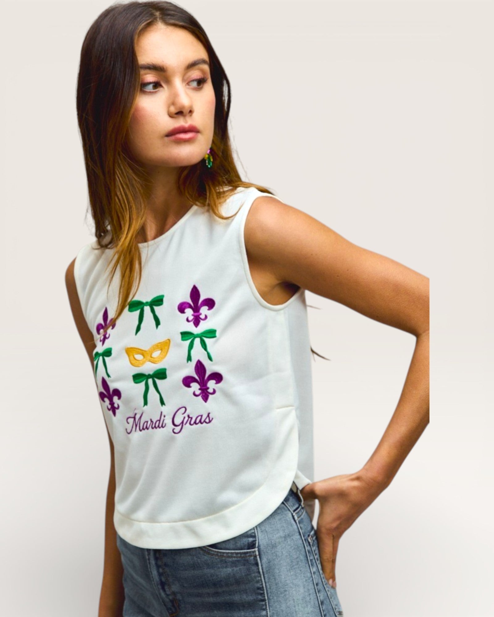 Woman wearing a white sleeveless top with colorful Mardi Gras designs on a plain background