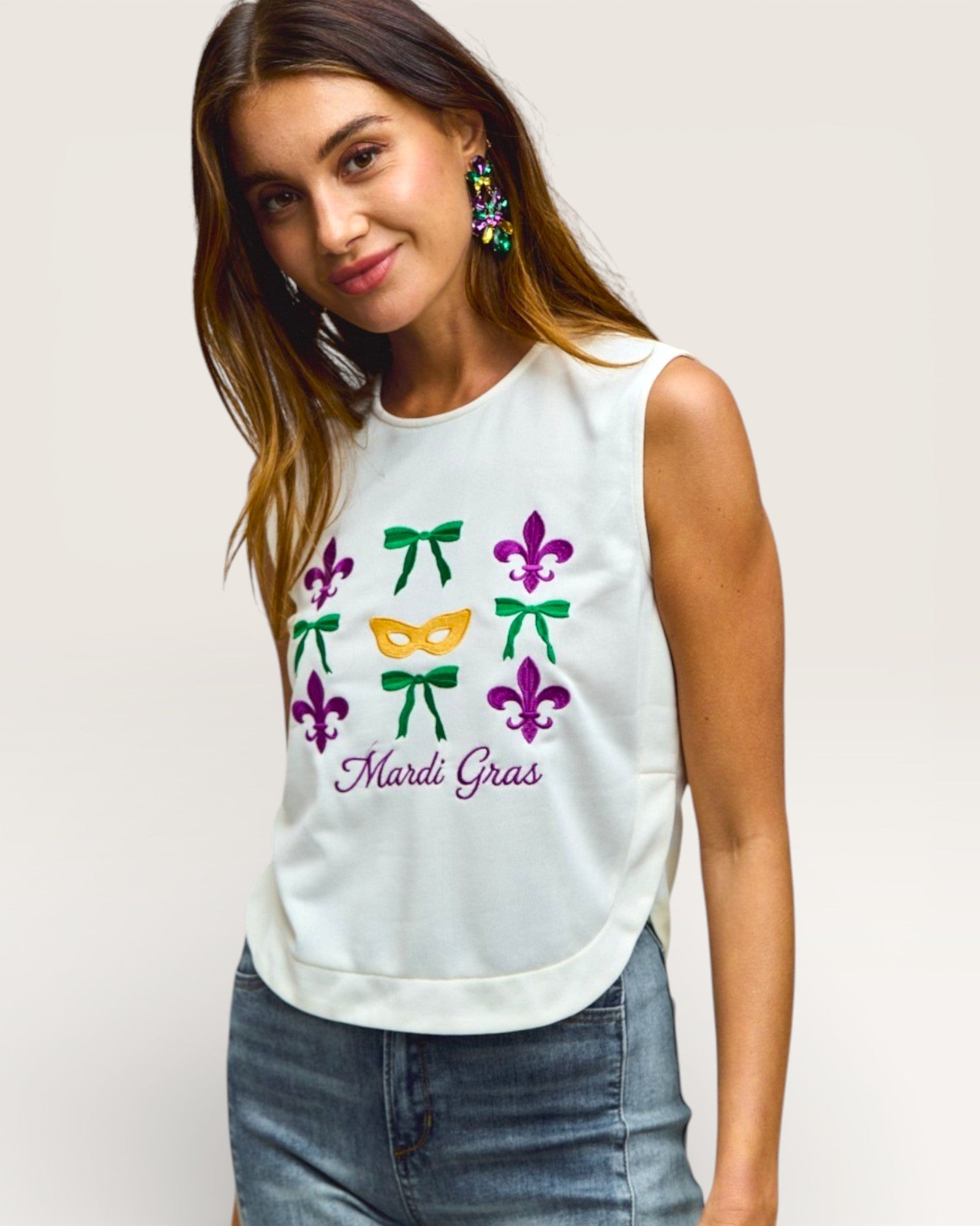 Woman wearing a white sleeveless top with Mardi Gras-themed designs on a plain background