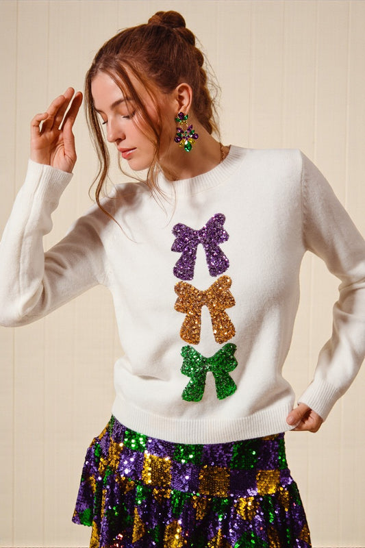 Woman wearing a white sweater with colorful bow designs and a multicolored skirt.