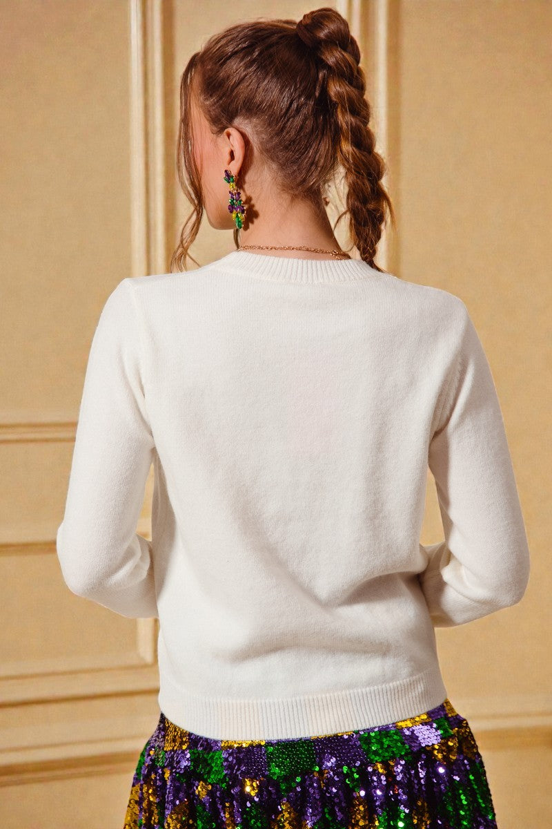 Person wearing a white sweater with a colorful skirt in front of a beige wall.