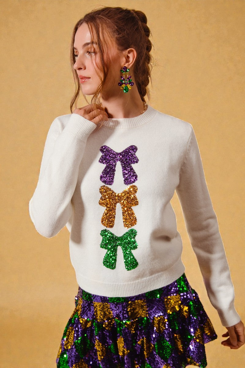 Woman wearing a white sweater with colorful sequin bows and a matching skirt against a beige background