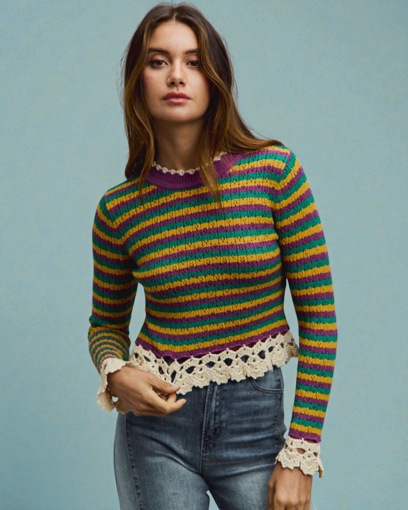 Woman wearing a colorful striped sweater with lace details on a light blue background
