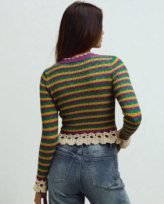 Person wearing a colorful striped sweater with lace details on a plain background