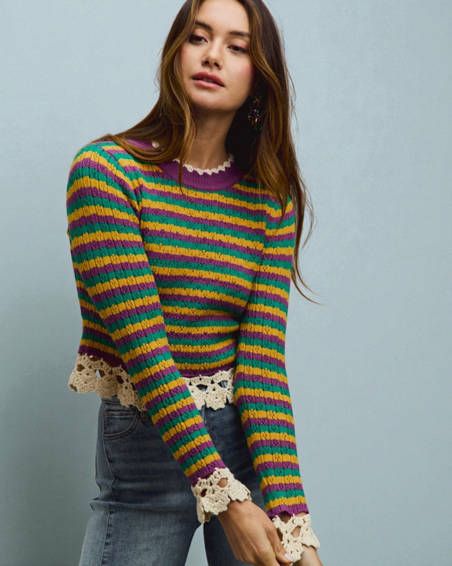 Woman wearing a colorful striped sweater with lace cuffs against a gray background