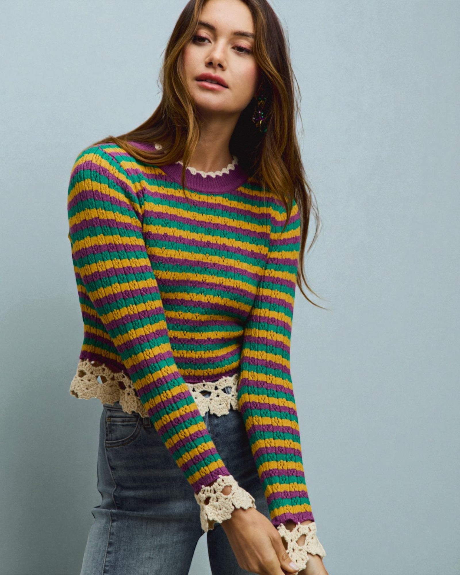 Woman wearing a colorful striped sweater with lace cuffs against a gray background