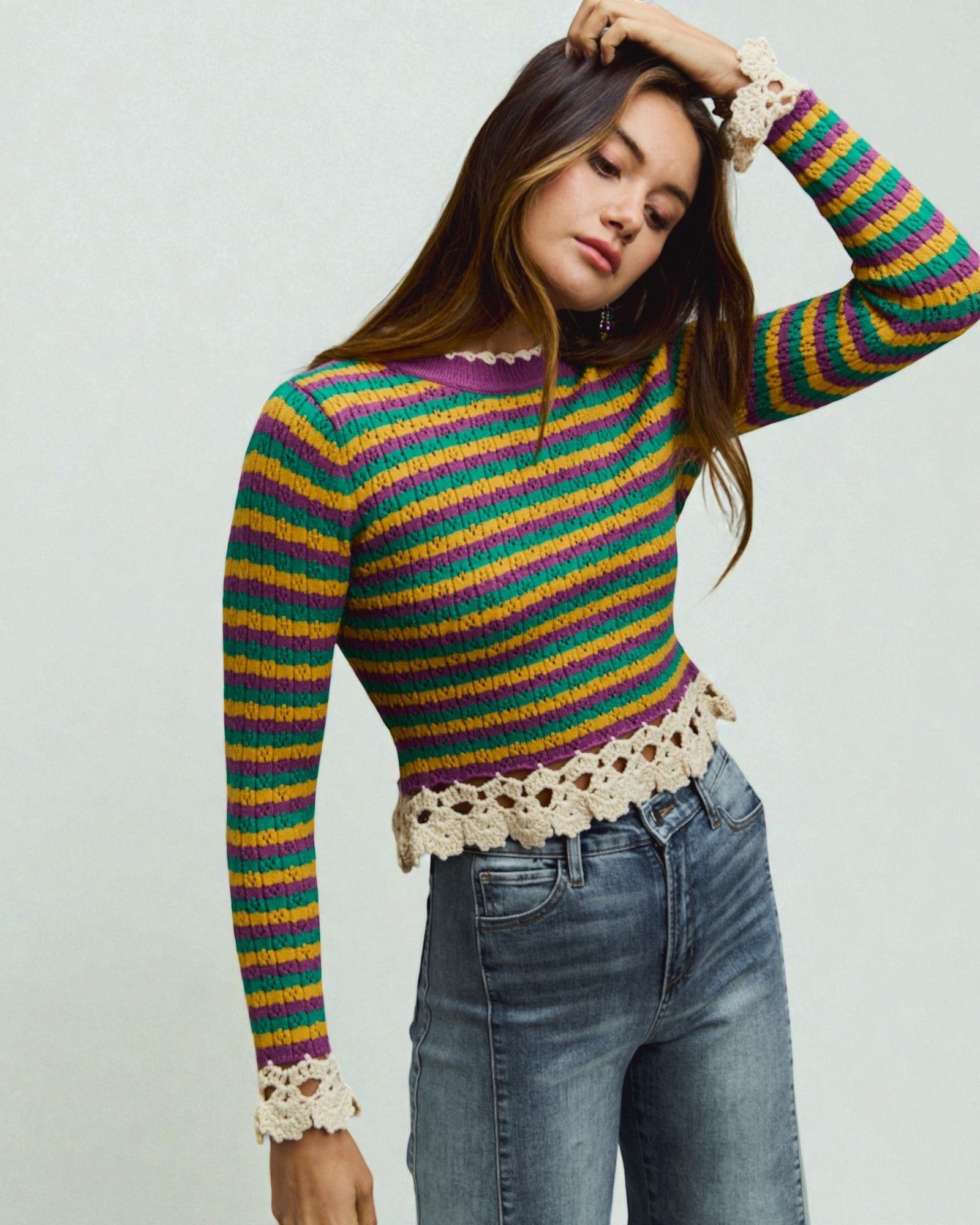 Woman wearing a colorful striped sweater with lace details on a plain background