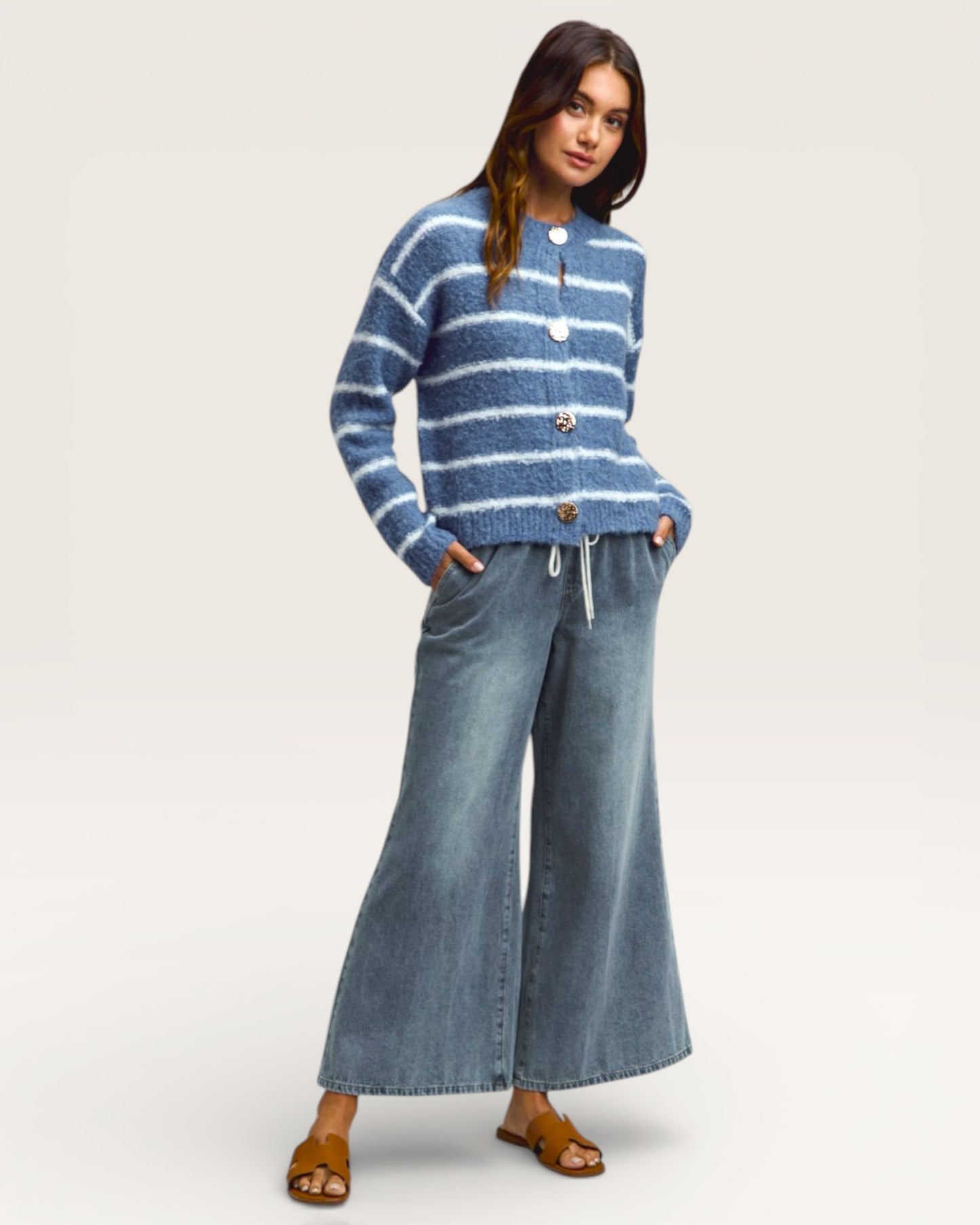 Woman wearing a blue striped sweater and wide-leg jeans on a white background
