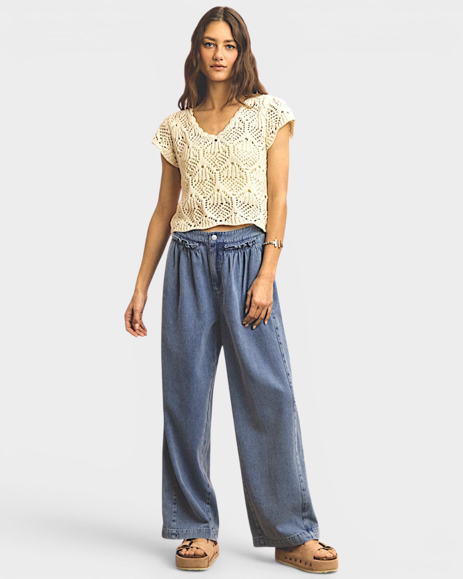 Woman wearing a beige lace top and blue wide-leg pants on a white background
