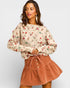 Woman wearing a floral blouse and brown skirt on a plain background