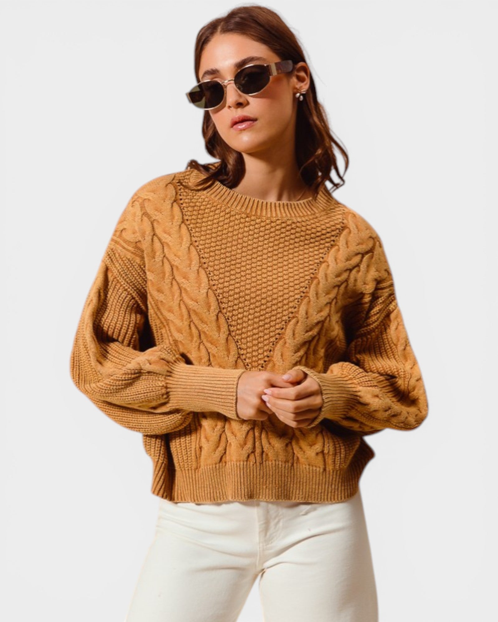Woman wearing a mustard yellow cable knit sweater and white pants on a plain background