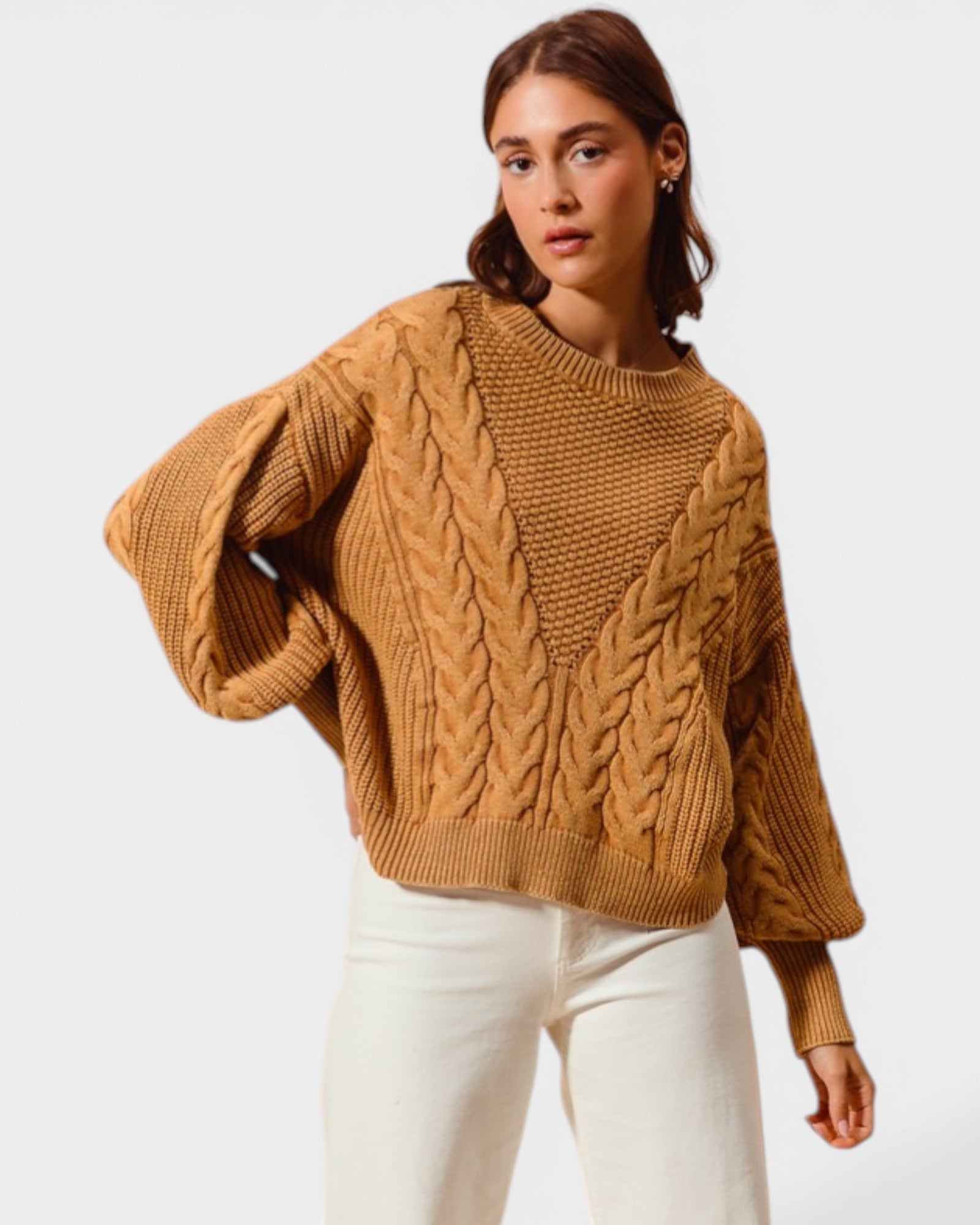 Woman wearing a brown cable knit sweater and white pants on a light gray background
