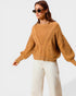 Woman wearing a mustard yellow cable knit sweater and white pants on a white background