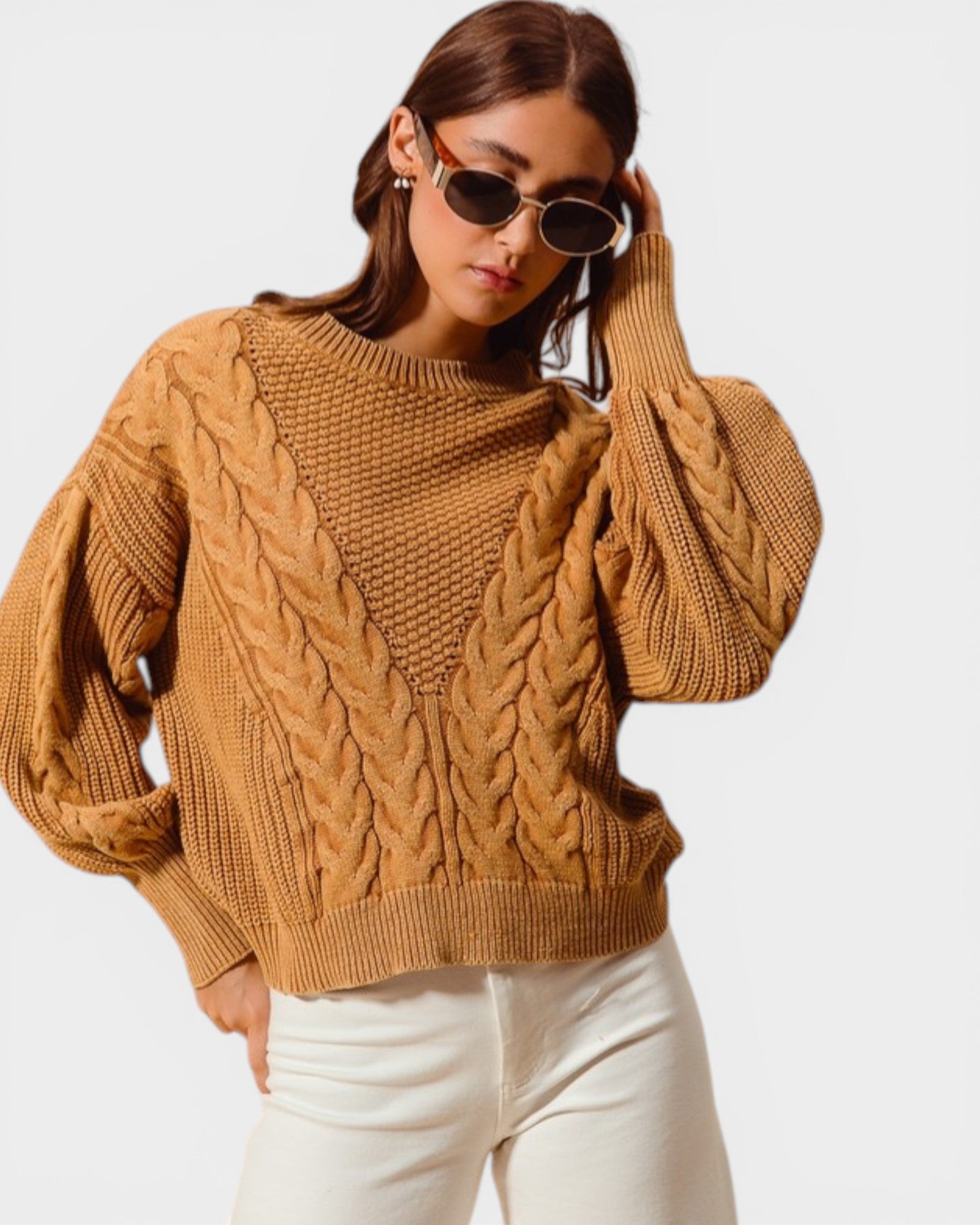 Woman wearing a brown cable knit sweater and white pants on a plain background