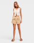 Woman wearing a white sleeveless top and beige shorts on a white background