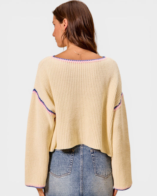 Woman wearing a beige sweater with colorful trim on a white background