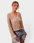 Woman wearing a beige crochet cardigan and denim shorts on a white background