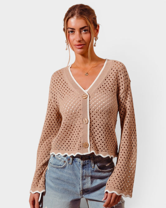 Woman wearing a beige open-knit cardigan and jeans on a plain background