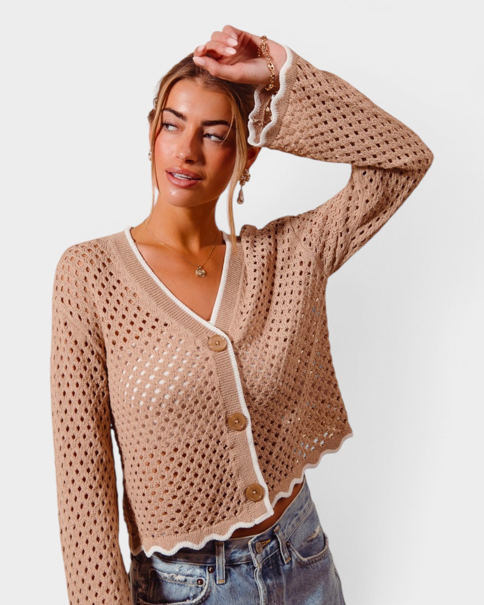 Woman wearing a beige crochet cardigan with white trim on a plain background